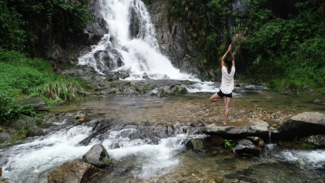 Aerial-view-of-healthy-lifestyle-woman-doing-yoga-near-waterfall-in-forest
