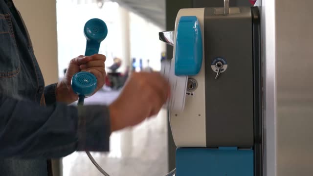 Asiatischer-Mann-mit-öffentlichen-Münztelefon-Festnetztelefon-innerhalb-des-internationalen-Flughafens.