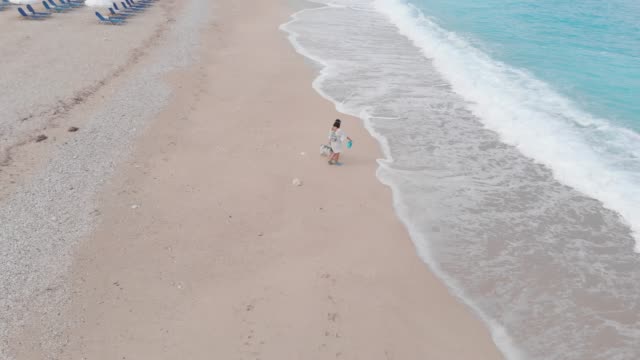 Mujer-caminando-con-su-perro-en-la-playa-en-la-mañana,-vista-aérea-drone