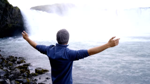 Hombre-joven-de-brazos-extendidos-delante-de-la-magnífica-cascada-en-Islandia