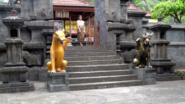 Eine-Frau-in-einem-langen-Rock-ergibt-sich-aus-einem-buddhistischen-Tempel-und-senkt-sich-eine-Steintreppe-mit-Statuen