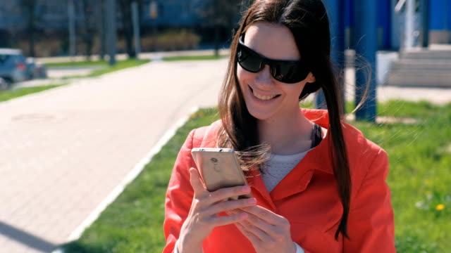Porträt-von-glücklich-Oung-Frau-im-roten-Mantel-wartet-auf-jemanden-und-überprüft-ihr-Handy-SMS.