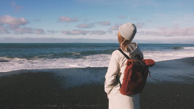 Tourist-woman-with-leather-bagpack-standing-near-the-coastal-landscape-in-Iceland.