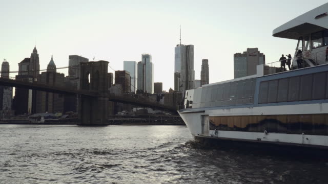 Lower-Manhattan-skyline-with-a-yacht-in-the-foreground-filmed-from-the-boat-in-the-East-River-under-the-Brooklyn-Bridge-in-New-York,-United-States