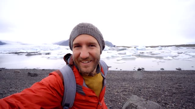 Young-man-taking-selfie-with-glacier-lake,-icebergs-floating-on-water-in-Iceland