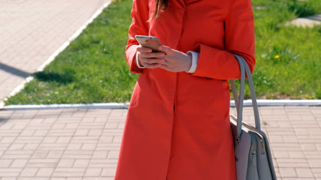 Nicht-erkennbare-Frau-im-roten-Mantel-wartet-auf-jemanden-und-überprüft-ihr-Handy-SMS.-Close-up-Hände.