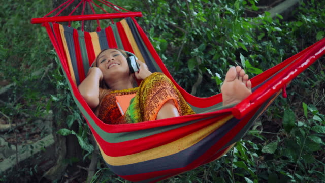 Young-woman-listening-to-music-on-a-hammock.
