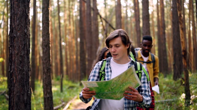 Glückliche-lächelnde-junge-Menschen-Touristen-gehen-in-Wald-mit-Papier-Karte-plaudern-und-lachen-genießen-Sie-Freiheit-und-Natur-und-tragen-Rucksäcke.