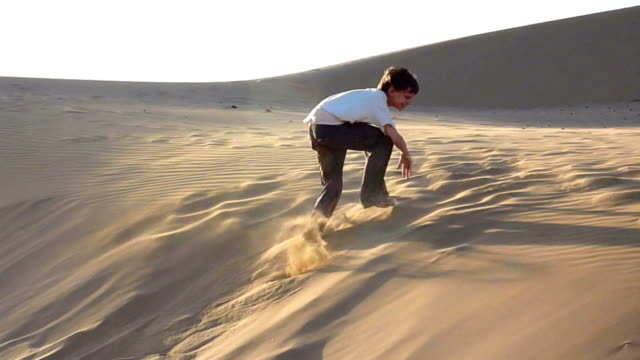 Boy-jumping-and-rolling-down-sanddune,-late-afternoon