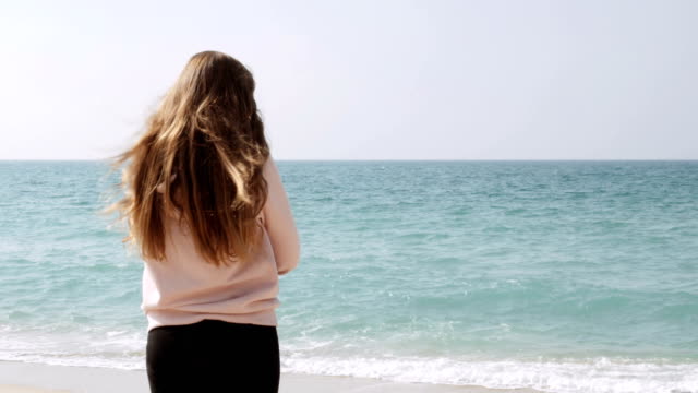 Chica-soñadora-con-largo-pelo-rojo-parado-en-la-playa-y-disfrutando-de-un-increíble-paisaje-marino,-brisa-marina-jugando-con-su-cabello.