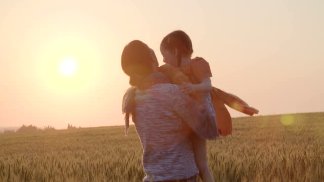 junge-asiatische-Familie-in-einem-Feld-mit-einem-Baby-1-Jahr-auf-der-Hand,-das-Konzept-von-Familienglück,-schöne-Sonne,-Sonnenuntergang,-Slow-motion