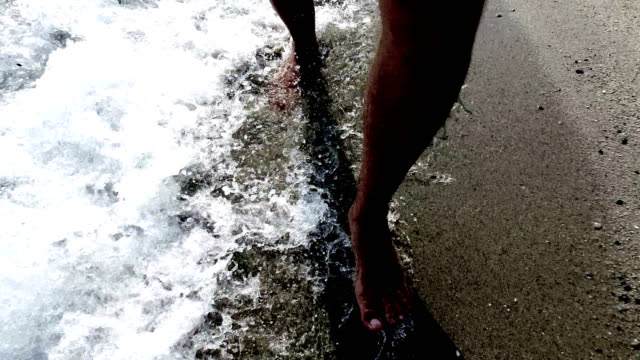 Men-barefoot-legs-silhouettes-walking-along-sea-shore-shallow-water-with-waves-splashing.-4k-trekking-steadicam--front-view-pov-shot