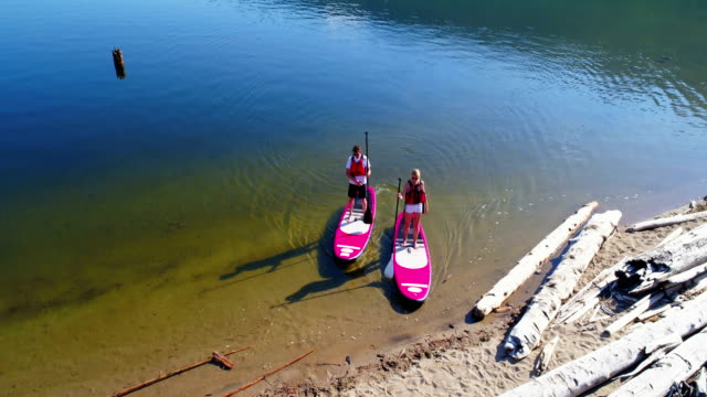 Couple-parking-paddleboard-at-riverbank-on-a-sunny-day-4k