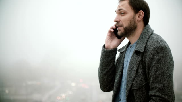 Young-man-standing-near-Eiffel-tower-in-Paris,-France-in-foggy-morning.-Male-talking-on-mobile-phone-with-somebody