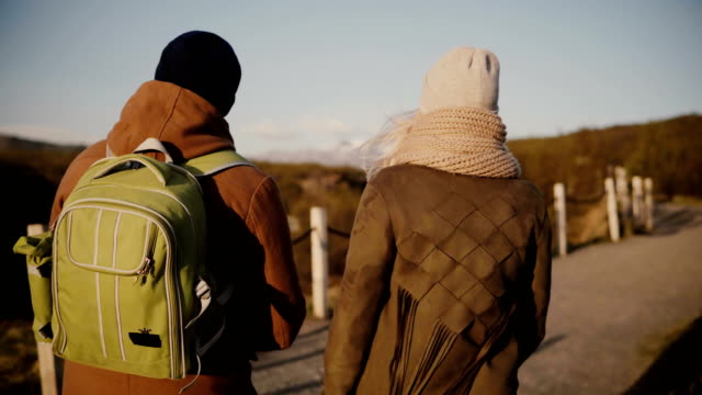 Back-view-of-traveling-young-couple-walking-on-the-nature,-valley.-Man-and-woman-hiking-in-Iceland-in-sunny-day