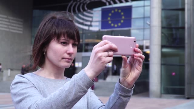 Turismo-de-mujer-toma-pictureson-smartphone-cerca-del-Parlamento-Europeo-en-Bruselas.-Bélgica