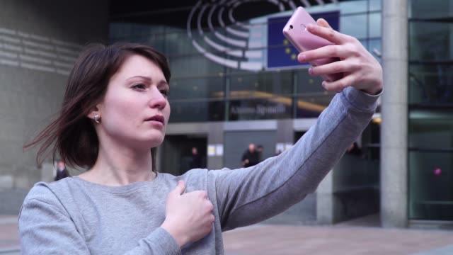 Señora-turismo-hacer-selfie-en-smartphone-cerca-del-Parlamento-Europeo-en-Bruselas.-Bélgica.-cámara-lenta