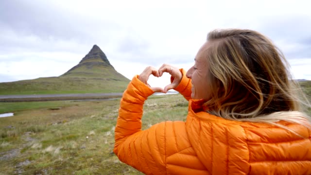 Junge-Frau-in-Island-machen-Herz-Formrahmen-Finger-am-berühmten-Berg-Kirkjufell
