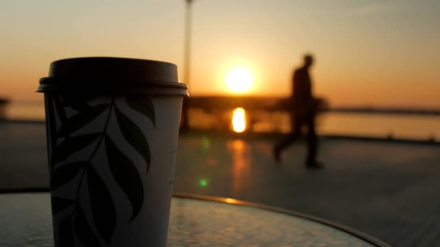 cups-with-coffee-are-standing-on-a-table-in-background-of-sunset,-female-hand-is-taking-one