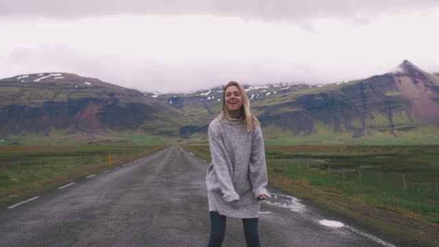Mujer-joven-feliz-bailando-en-el-camino-de-asfalto-en-Islandia-y-divertirse,-cámara-lenta