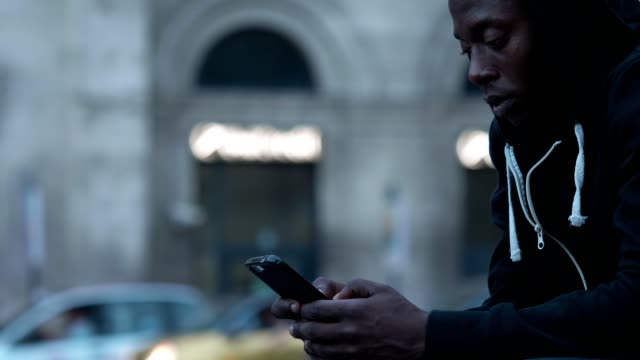 Junge-schwarze-Amerikaner-konzentrierte-sich-auf-das-Schreiben-auf-seinem-Smartphone-in-das-Profil-der-Stadt