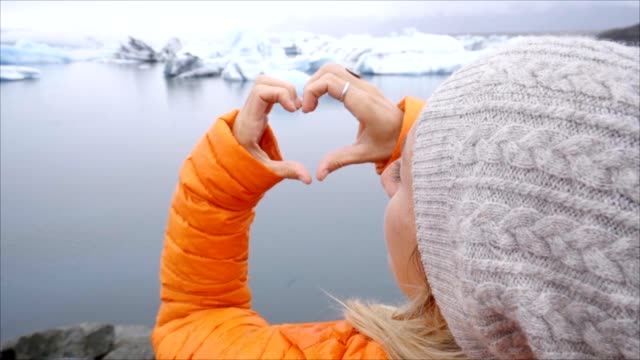 Young-woman-making-heart-shape-finger-frame-on-glacier-lagoon-in-Iceland-showing-love-and-compassion-to-nature
