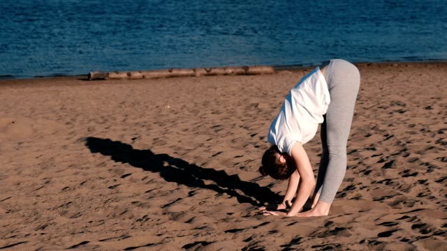Woman-doing-yoga-on-the-beach-by-the-river-in-the-city.-Beautiful-view-in-Padangustasana-pose.