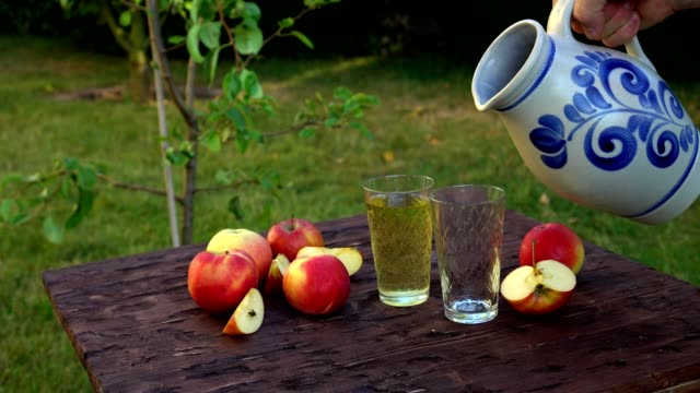 Traditional-apple-wine-in-the-city-of-Frankfurt-in-Hesse.-A-jug-of-wine-is-on-an-old-wooden-table-in-the-garden,-around-it-are-apples