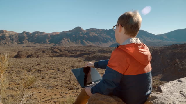 ein-junger-Mann-mit-einem-Laptop,-umgeben-von-vulkanischen-Berglandschaft