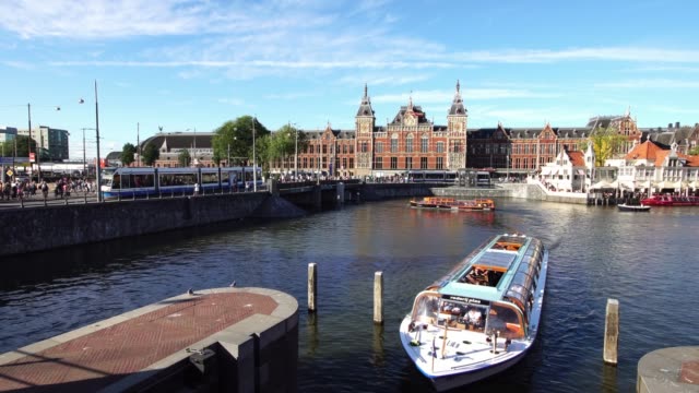 Icónica-escena-holandesa,-barco-turístico-en-el-centro-de-la-canal-por-la-estación-Central-de-Ámsterdam,-de-Europa.