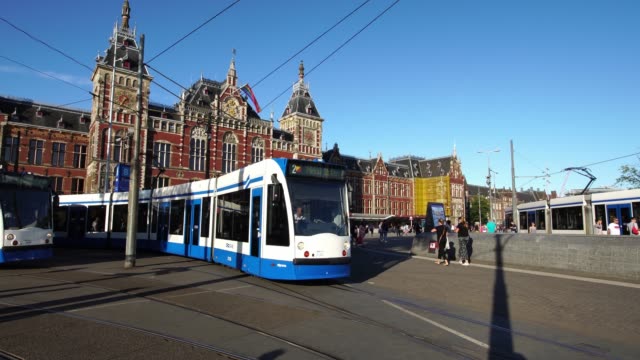 Tram-commuter-train-departs-Central-Railway-Station-in-downtown-Amsterdam,-Europe.