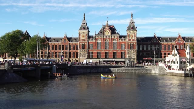 Traditional-boats-at-canal-waterfront-in-front-of-Amsterdam-Central-station,-Europe.