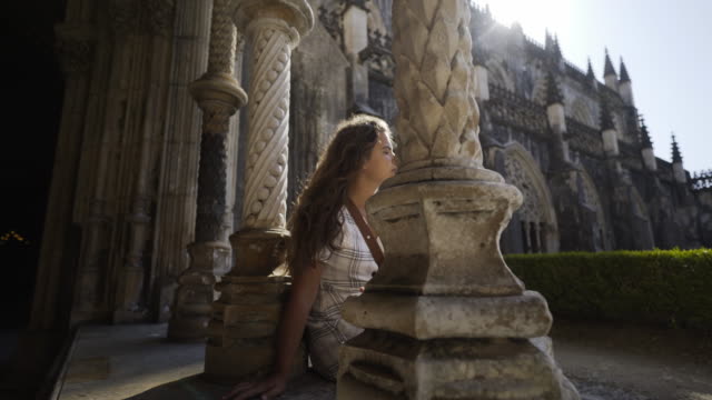 Young-woman-sitting-near-pillars-of-old-building