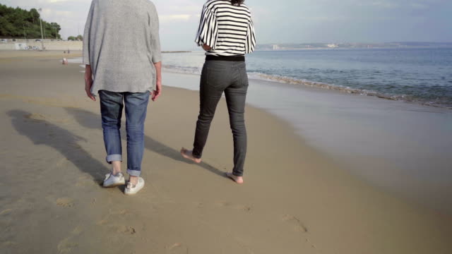 Mujeres-maduras-caminando-en-arena-húmeda-a-orilla-del-mar.