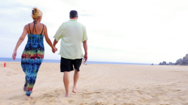 An-older-couple-holding-hands-and-walking-on-the-beach