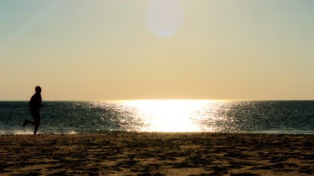male-runner-running-on-beach,-sunset-silhouette,-slow-motion