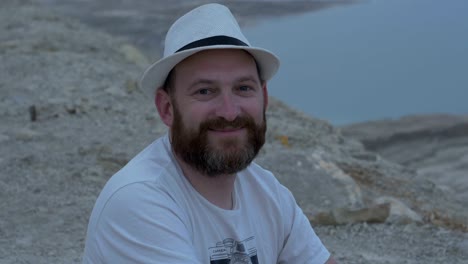 Bärtiger-Mann-vierzig-Jahre-in-einem-Hipster-Hut,-der-in-die-Kamera-schaut,-auf-dem-Hintergrund-des-Toten-Meeres,-Israel