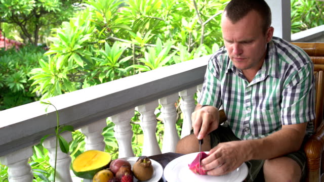 Man-sitting-on-the-balcony-cleans-the-Pitahaya-fruit-and-eats