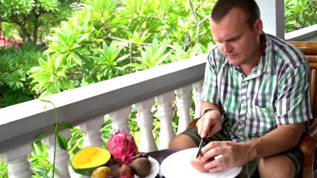 Man-sitting-on-the-balcony-cleans-the-passion-fruit-and-eats