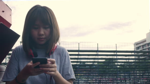 Schöne-junge-asiatische-Frau-anhören-von-Musik-auf-einem-Smartphone-in-der-Stadt.-Junge-asiatische-Frau,-entspannende-Musik-hören-auf-der-Straße.