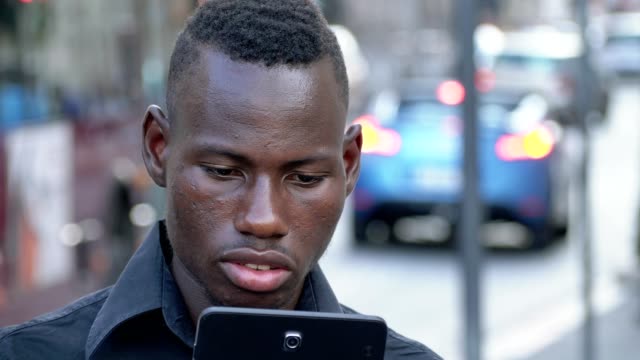 Smiling-american-african-young-man-typing-on-his-smartphone-outdoor