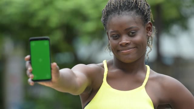 Young-happy-African-woman-showing-phone-outdoors