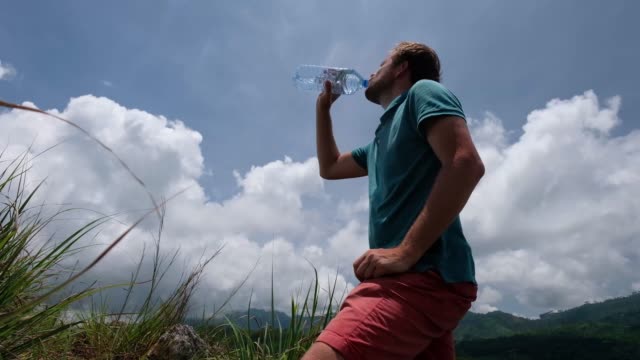 Young-man-drinking-bottle-of-water-standing-outdoor-in-hot-summer