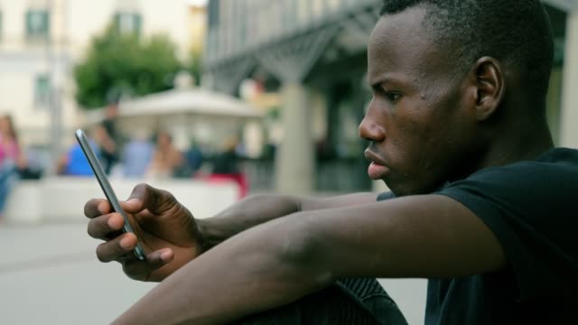 attraktive-junge-schwarze-Afrikaner-konzentrierte-sich-auf-das-Schreiben-auf-Smartphone-Outdoor-