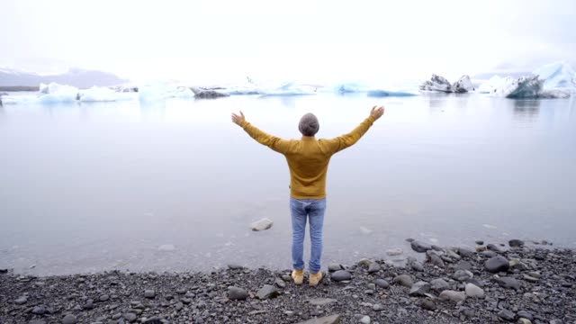 Junger-Mann-an-die-Gletscherlagune-Islands-ausgestreckte-Armen