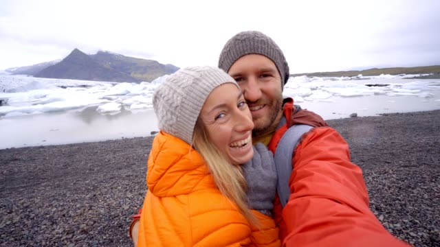 4-K-Video-der-jungen-Paare,-die-Spaß-unter-Selfie-durch-den-Gletschersee-Jökulsárlón-Lagune-in-Island.-Zwei-Personen-Reisen-Liebe-Romantik-Kommunikationskonzept-miteinander-teilen.-Frühling,-Kälte