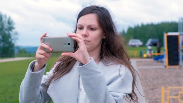 Junge-Frau-schießt-ein-Foto-und-Video-auf-einem-Mobiltelefon-auf-dem-Spielplatz.