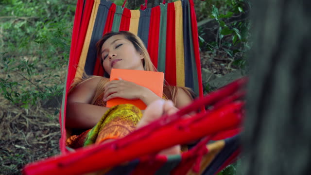 Young-woman-laying-down-on-hammock-and-reading-a-book