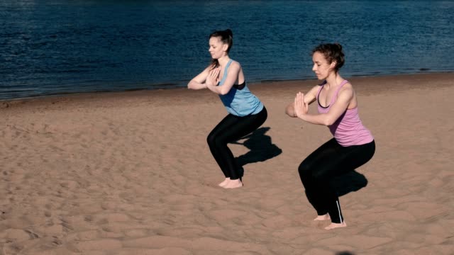 Zwei-Frau-Yoga-am-Strand-am-Fluss-in-der-Stadt-zu-tun.-Schöne-Aussicht.-Utkatasana-Pose.