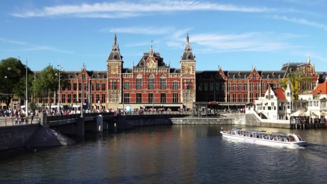 Tourist-boats-at-center-canal-waterfront-in-front-of-Amsterdam-Central-station,-Europe.